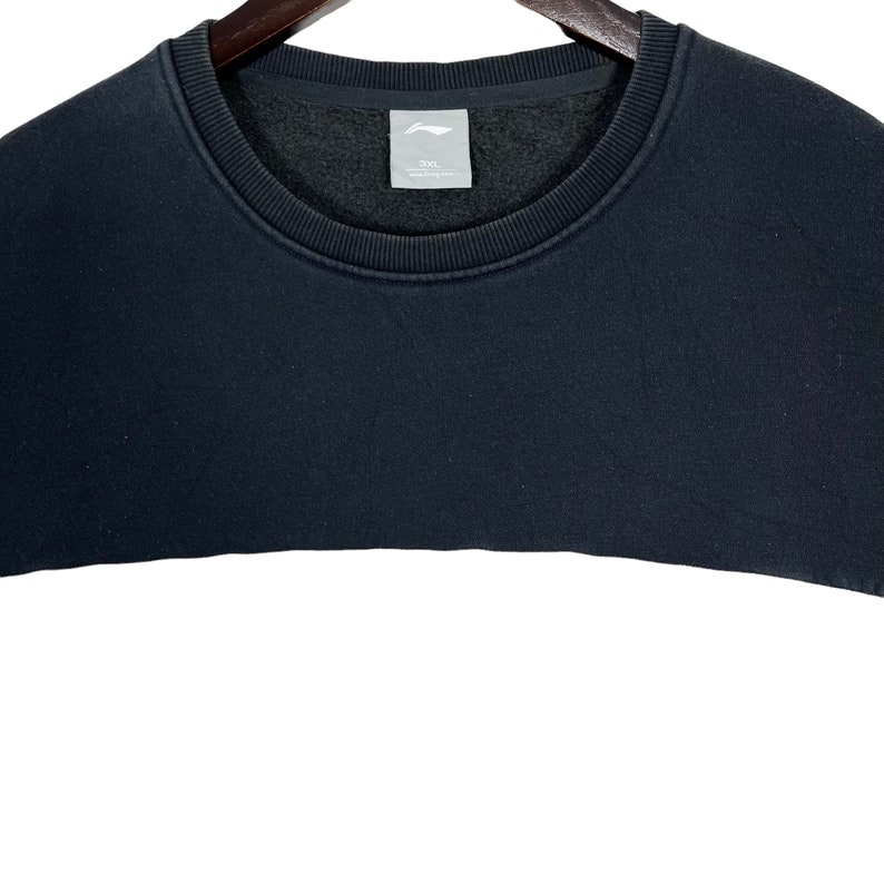 May include: Black sweatshirt with a crew neck and a white label with the text "2XL" on the front.