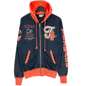 May include: A navy blue zip-up hoodie with an orange hood lining and accents. The hoodie features a devil mascot patch, the text "The Legend Of Devil Soul '06", and the word "Titans" on the sleeve. The hoodie is hanging on a black hanger.