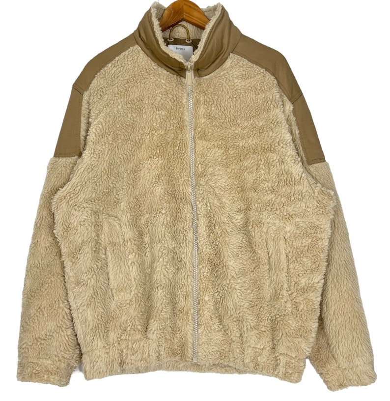 May include: A beige fleece jacket with brown leather accents on the shoulders and sleeves. The jacket has a zipper closure and a stand-up collar.