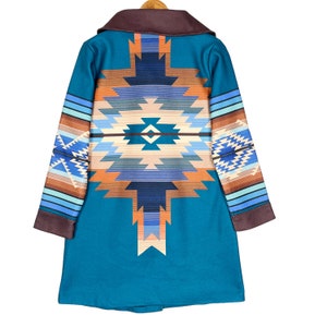 Może przedstawiać: Długi, turkusowy płaszcz z długimi rękawami, ozdobiony geometrycznym wzorem w odcieniach brązu, pomarańczy, błękitu i bieli. Wzór przypomina wzory indiańskie.