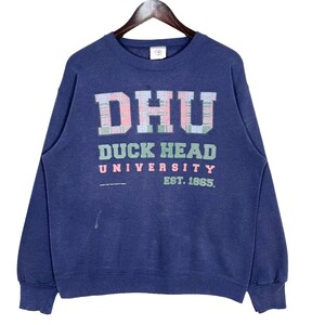 May include: Navy blue sweatshirt with the text "DHU DUCK HEAD UNIVERSITY EST. 1865" in a plaid design. The sweatshirt is hanging on a wooden hanger.