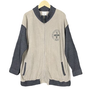 Może przedstawiać: Beżowa i szara kurtka zapinana na zamek błyskawiczny z czarno-białym logo z napisem "Urban Search and Rescue USAR".