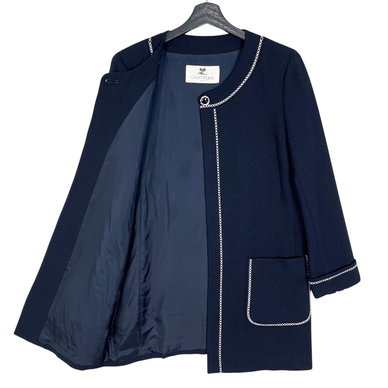 May include: A navy blue blazer with a white trim around the neckline, cuffs, and pockets. The blazer has a single button closure and a label that reads "Courr&egrave;ges".
