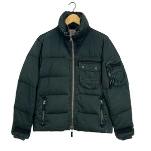 May include: A dark green puffer jacket with a zipper closure and multiple pockets. The jacket has a quilted design and a high collar.