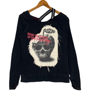 May include: Black long-sleeved sweatshirt with a distressed graphic of a skull inside an apple with the text "Falcons Have the Thrill of the Fatal Dose". The sweatshirt has a zip detail on the shoulder.