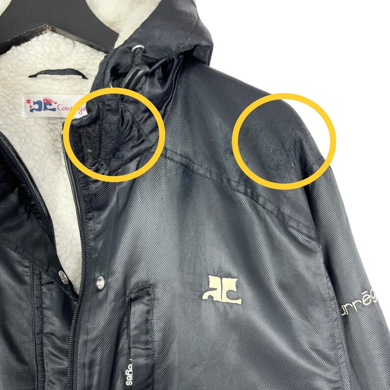 May include: Black hooded jacket with a white fleece lining. The jacket has a zipper closure and two pockets. The jacket has a logo on the left chest and the text "unnea" on the right sleeve.