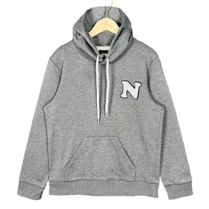 May include: A gray hoodie with a white drawstring and a front pocket. The hoodie features a white and navy blue letter "N" patch on the chest. The hoodie is displayed on a wooden hanger.
