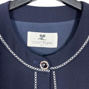 May include: A navy blue blazer with a white stitched trim around the collar and button placket. The blazer has a single button closure and features a white label with the text "Courr&egrave;ges Paris" on the front.