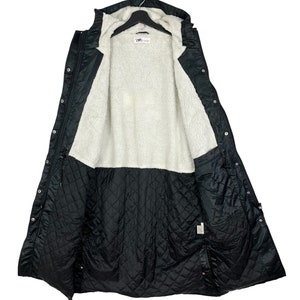 May include: A black long-sleeved jacket with a hood, lined with white fleece and a quilted interior. The jacket has a button closure and multiple pockets.
