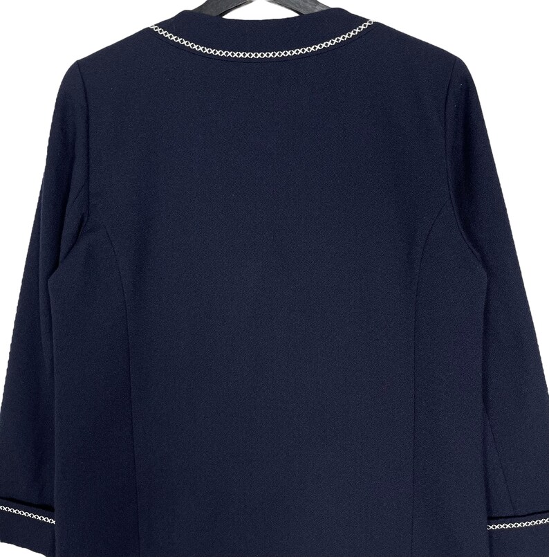 May include: A navy blue blazer with a white chain trim around the neckline and cuffs.