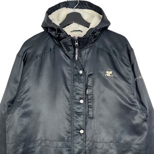 May include: Black hooded jacket with a fleece lining. The jacket has a zipper closure and a button placket. The jacket has a logo on the left chest and the word "Courage" on the zipper.