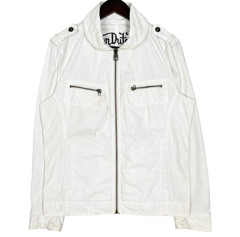 K&ouml;nnte beinhalten: Eine wei&szlig;e Rei&szlig;verschlussjacke mit Stehkragen und zwei Pattentaschen auf der Vorderseite. Die Jacke hat ein "Von Dutch" Logo auf der Vorderseite.