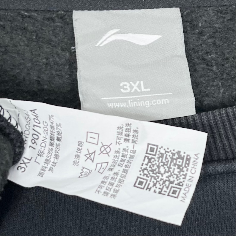 May include: White tag with black text and a black and white logo. The tag has the text "3XL 190/104A", "www.lining.com", "3XL", and "MADE IN CHINA". The tag also has a QR code and washing instructions.