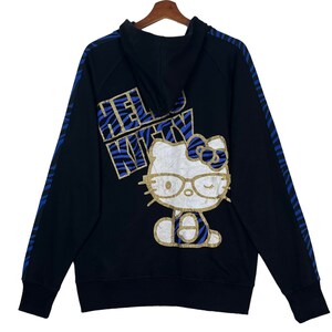 May include: Black hooded sweatshirt with a blue and gold Hello Kitty graphic on the back. The graphic features Hello Kitty wearing glasses and a headband with a bow.