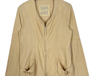 Puede incluir: Una chaqueta amarilla clara con cremallera, mangas largas y dos bolsillos. La chaqueta tiene una etiqueta que dice "Le  Atelier  Marithé  François  Girbaud".
