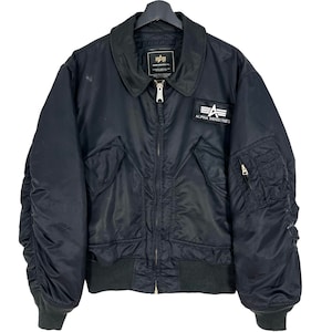 May include: A black bomber jacket with a zip fastening and a patch on the left chest that reads "ALPHA INDUSTRIES".