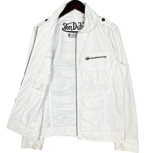 K&ouml;nnte beinhalten: Wei&szlig;e Rei&szlig;verschlussjacke mit einem Von Dutch Logo auf der Vorderseite. Die Jacke hat einen Stehkragen und zwei Taschen auf der Vorderseite.