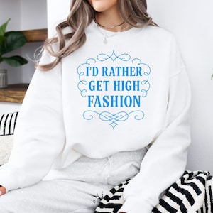 Puede incluir: Sudadera blanca con el texto "I'D RATHER GET HIGH FASHION" en una fuente decorativa azul. La sudadera es lisa y tiene cuello redondo. La imagen es de una persona que lleva la sudadera.