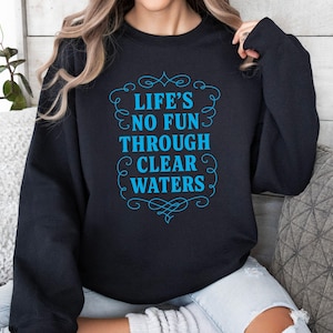 Puede incluir: Sudadera negra con el texto "LIFE'S NO FUN THROUGH CLEAR WATERS" en turquesa dentro de un marco decorativo. La sudadera es de color negro liso y tiene mangas largas. El texto está en una fuente estilizada.