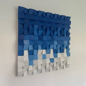 May include: A wall art piece made of wooden blocks, painted in shades of blue and white. The blocks are arranged in a wave-like pattern, creating a modern and abstract design.