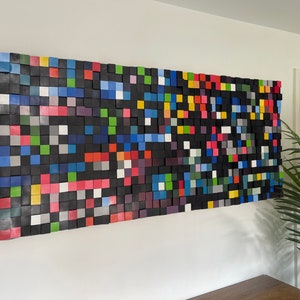 May include: A large abstract wall art piece made of colourful wooden squares. The squares are arranged in a random pattern, creating a dynamic and modern look. The piece is perfect for adding a touch of colour and interest to any room.