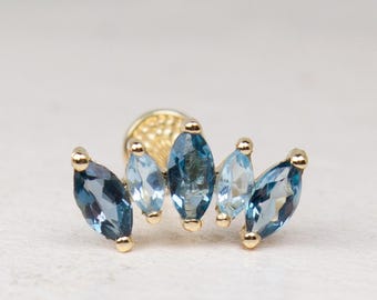 Könnte beinhalten: Ein goldfarbener Ohrstecker mit fünf hellblauen, marquiseförmigen Edelsteinen. Die Edelsteine sind fächerförmig angeordnet, mit drei zentralen Steinen und zwei seitlichen. Der Ohrstecker hat einen Stecker und einen Verschluss für sicheren Halt.