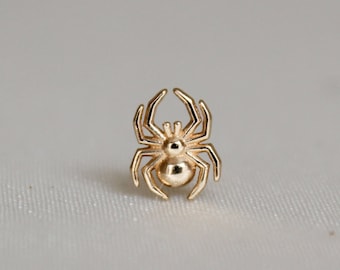May include: A small, gold-colored spider charm with detailed legs and body. The spider is centered on a white background. This charm could be used for jewelry making or as a decorative element.