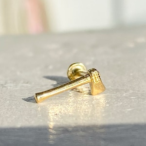 Op de afbeelding: Gouden oorbel in de vorm van een bijl. De oorbel is een klein, gedetailleerd replica van een bijl.