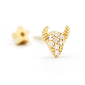 May include: A pair of gold earrings. One is a star shape, the other a bull's head with clear, sparkling stones. The bull's head earring has a textured horn design and a post backing. The earrings are set against a white background.