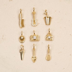 May include: Ten gold charms with clear crystal accents. The charms include a comb, guitar, cup with a straw, baseball cap, camera, purse, saw, shovel, and tennis racket.