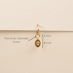 Pu&ograve; includere: Orecchino a cerchio dorato con un piccolo ciondolo di forma ovale. Il ciondolo ha un design a forma di sole con un centro rialzato. Il diametro interno dell'anello &egrave; di 3 mm, il ciondolo misura 8 mm di lunghezza e 4 mm di larghezza.