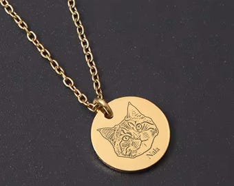 May include: A gold-colored necklace with a circular pendant featuring an engraved cat portrait and the name "Nala." The chain and pendant are a matching gold tone. The cat's face is detailed with etched lines.