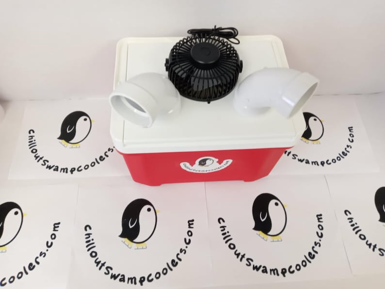 May include: A red and white cooler with a black fan and two white elbow-shaped vents. The cooler has a penguin logo and the text "chilloutswampcoolers.com" is printed on the surrounding surfaces.