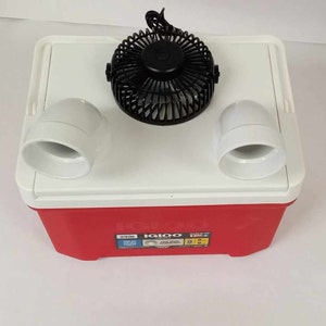 May include: A red and white Igloo cooler with a black fan and two white air vents attached to the top. The cooler has a red base and a white lid. The fan is centered on the lid, and the vents are on either side.