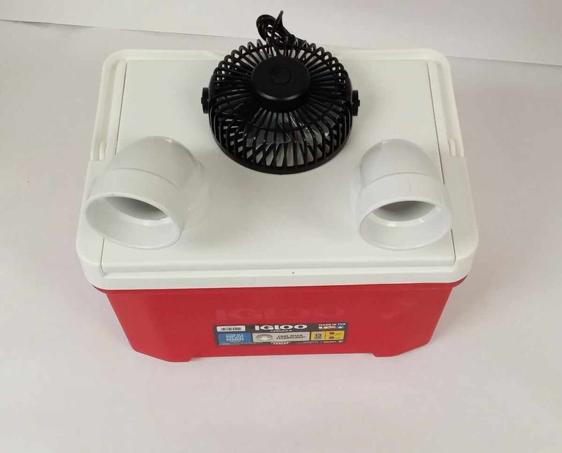 May include: A red and white Igloo cooler with a black fan and two white air vents attached to the top. The cooler has a red base and a white lid. The fan is centered on the lid, and the vents are on either side.