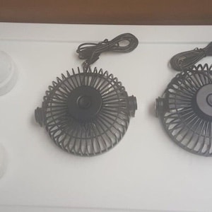 May include: Two black electric fans with white cords and white plastic connectors. The fans are on a white surface.