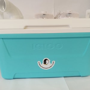 May include: A blue Igloo cooler with a white lid and two fans on top. The cooler has a sticker on the front that says "Chillout Swamp Coolers.com".