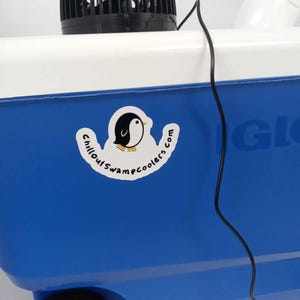May include: A blue and white cooler with a black fan on top. A sticker with a penguin logo and the text "Chillout Swampcoolers.com" is on the side. A black power cord extends from the fan.