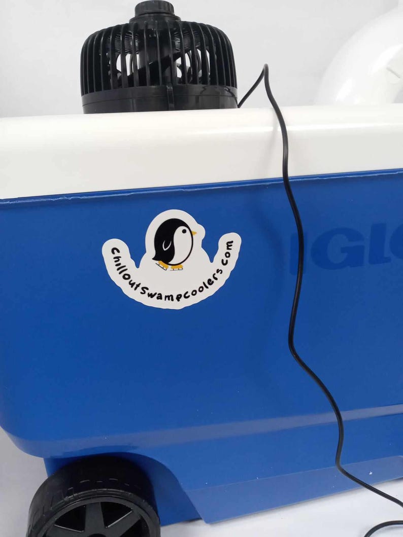 May include: A blue and white cooler with a black fan on top. A sticker with a penguin logo and the text "Chillout Swampcoolers.com" is on the side. A black power cord extends from the fan.
