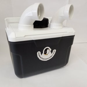 May include: A black and white cooler with a white lid and two white PVC pipes attached to the top. The cooler has a sticker on the side that says "Chilloutcampcoolers.com" and features a cartoon penguin.