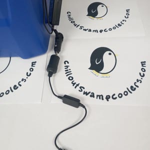Peut inclure: Un cordon d'alimentation noir avec un connecteur USB, un adaptateur de voiture et un petit bo&icirc;tier noir. Le cordon est connect&eacute; &agrave; une glaci&egrave;re bleue. Le texte "ChilloutSwampcoolers.com" est imprim&eacute; sur du papier blanc.