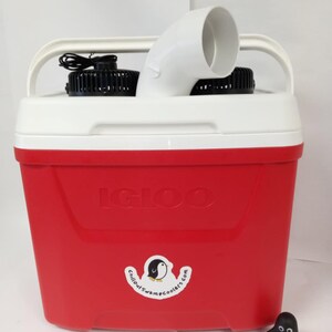 May include: A red Igloo cooler with two black fans and a white vent pipe. The cooler has a sticker that says "Chillout Swamp Coolers.com" with a penguin logo. A small penguin figurine is in the foreground.