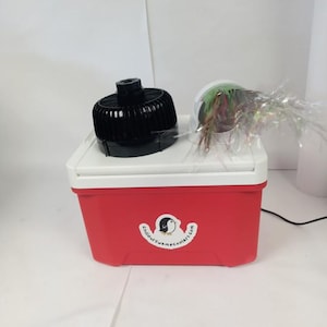 May include: A red and white cooler with a black fan and a decorative item on top. The cooler has a logo that says "Chillout SwampCoolers.com". The fan is black and round. The decorative item is a clear container with colorful accents.