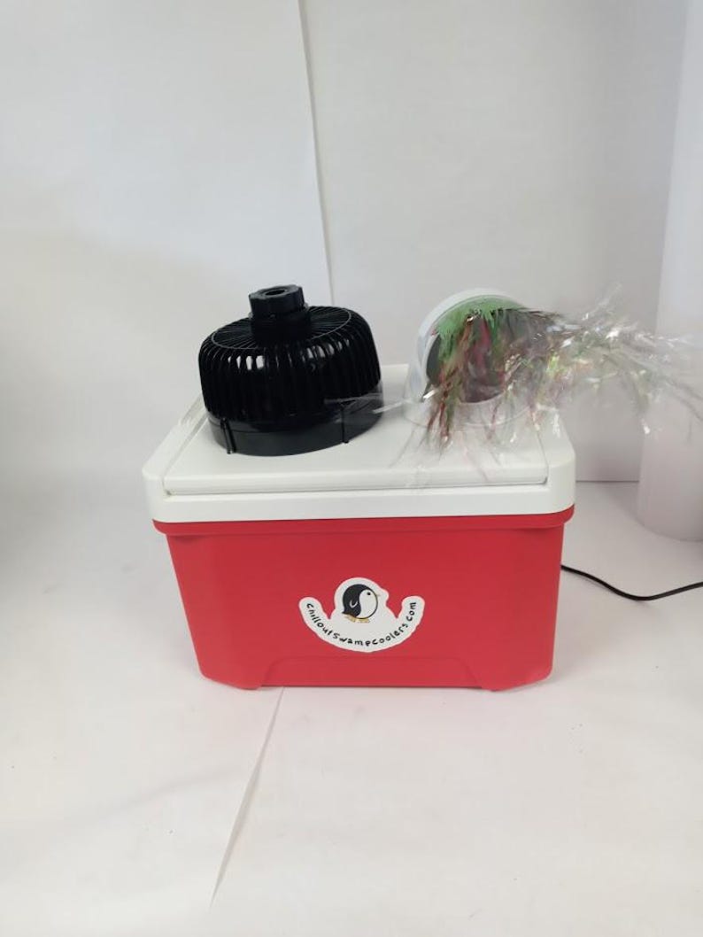 May include: A red and white cooler with a black fan and a decorative item on top. The cooler has a logo that says "Chillout SwampCoolers.com". The fan is black and round. The decorative item is a clear container with colorful accents.