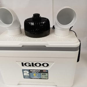 Puede incluir: Una nevera blanca Igloo con un ventilador negro y dos tubos de ventilaci&oacute;n blancos en la parte superior. La nevera tiene una pantalla digital de temperatura que muestra 25 grados Fahrenheit. La nevera est&aacute; etiquetada como "Igloo Ultra 25 Qt."
