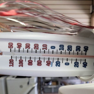 May include: A white thermometer displaying both Fahrenheit and Celsius scales. The temperature reads approximately 40&deg;F and 4&deg;C. The thermometer has red and blue markings, with the word "FREEZE" visible.
