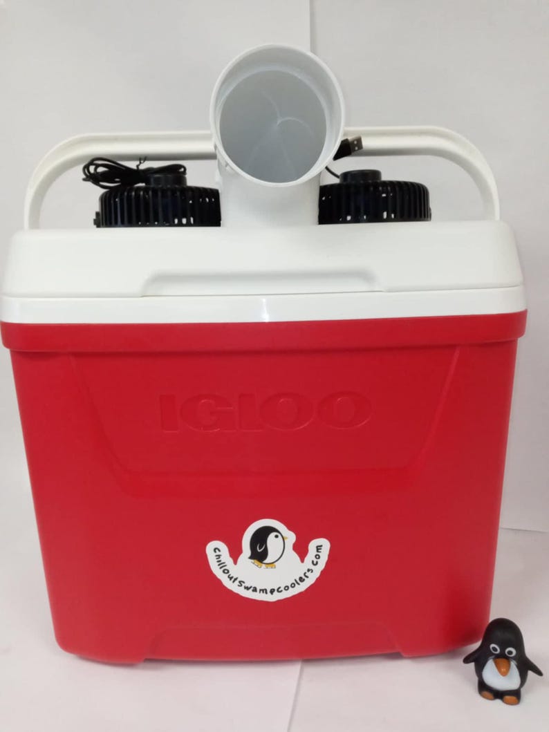 May include: A red Igloo cooler with two fans and a white tube on top. The cooler has a sticker that says "chilloutswamcoolers.com" with a penguin logo. A small penguin figurine is in the foreground.