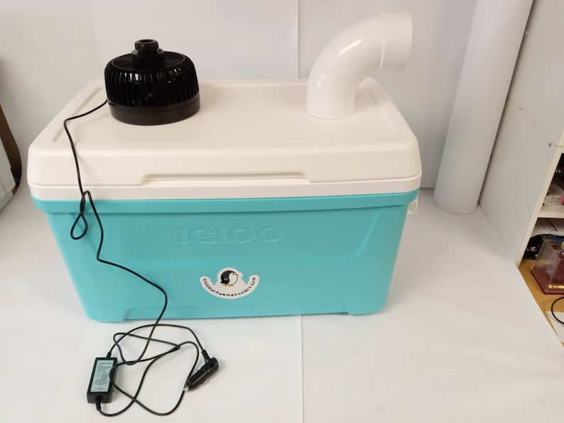 May include: A blue Igloo cooler with a white lid and a black fan on top. A white PVC pipe is attached to the cooler. A black power cord is connected to the fan and a black power adapter is on the floor.