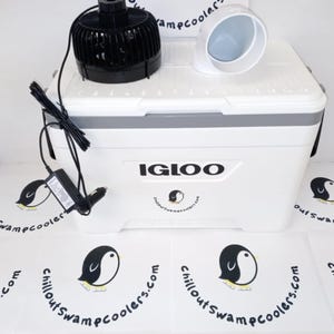 May include: A white Igloo cooler with a black fan and a white air vent on top. The cooler has a gray trim and the text "IGLOO" on the front. The image also shows a power adapter and several logos with a penguin.