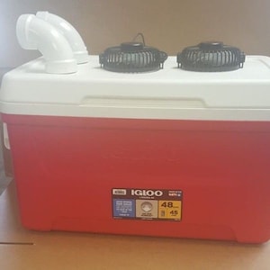 May include: Red Igloo cooler with two black fans on top and white PVC pipes on the side. The cooler has a white lid and a sticker that says "Igloo Leisure 48 QT" with the numbers "48" and "45" circled.